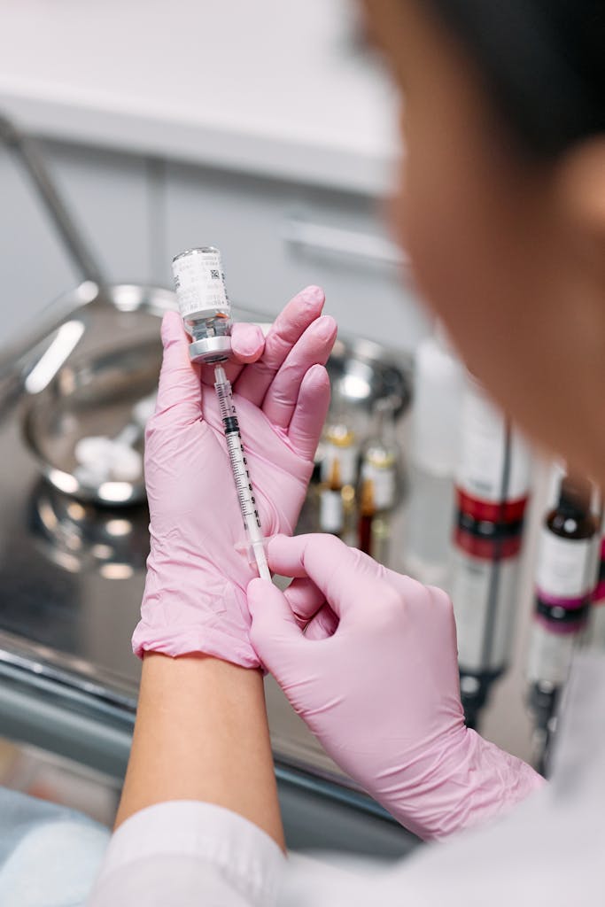 A healthcare worker wearing gloves prepares a syringe with medication in a clinical setting.