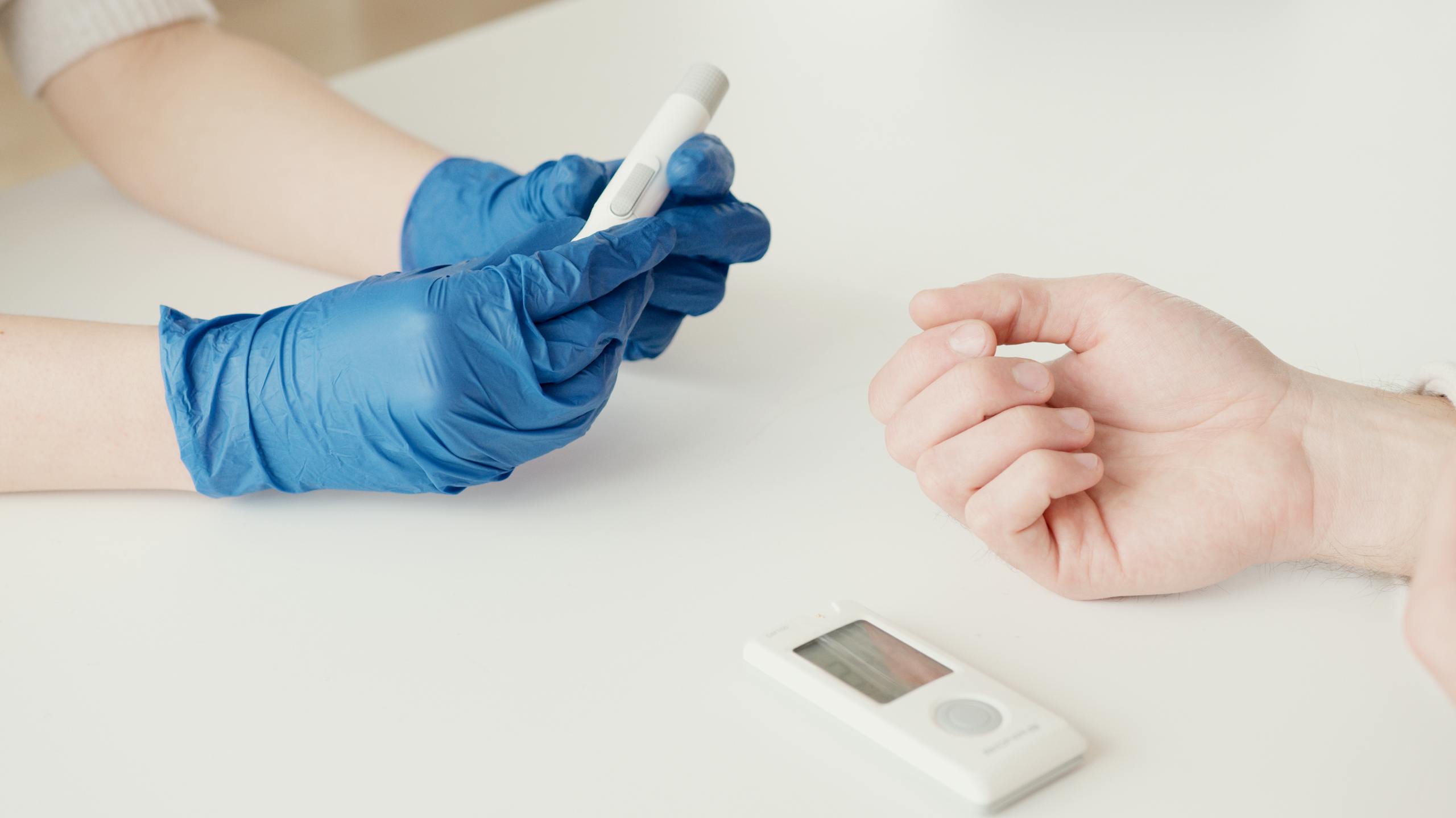 A healthcare worker uses a glucometer to check blood sugar levels in an indoor setting.