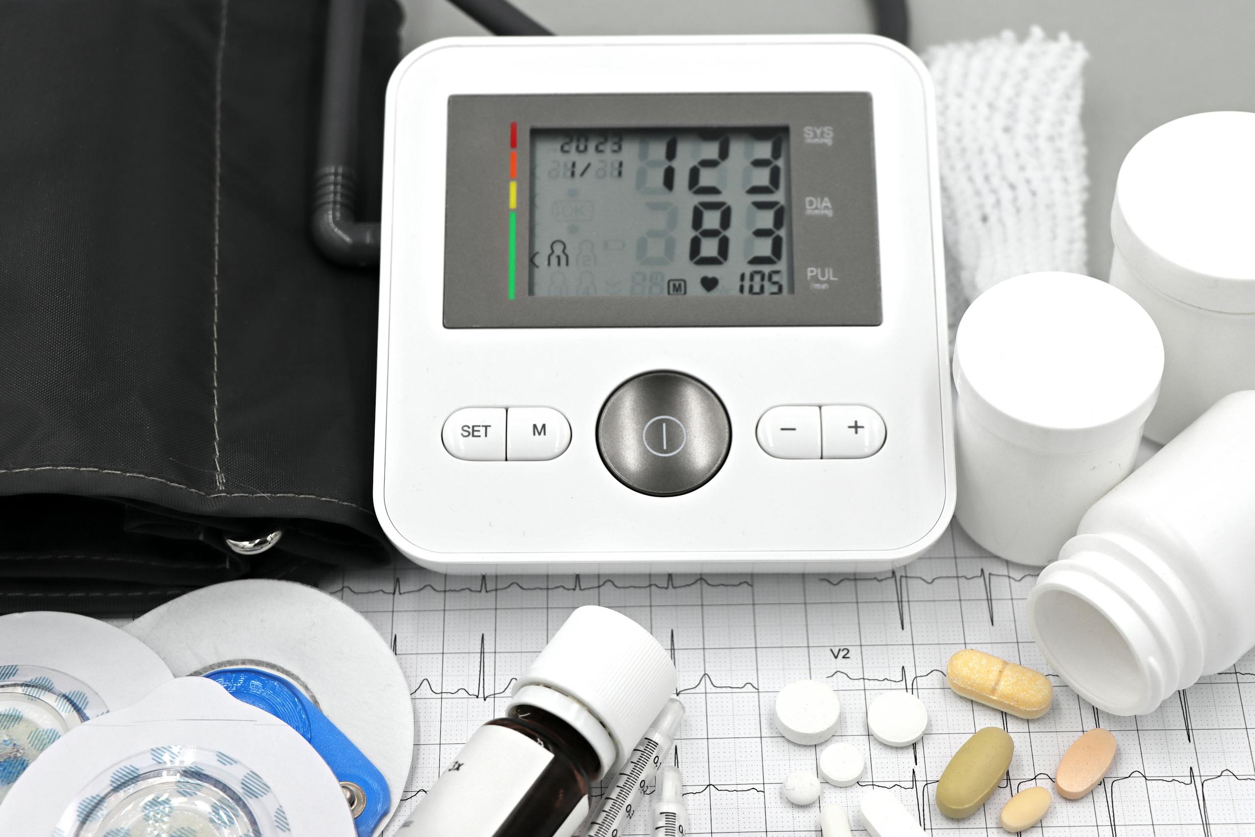 Close-up of medical equipment including blood pressure monitor, pills, and ECG printout.